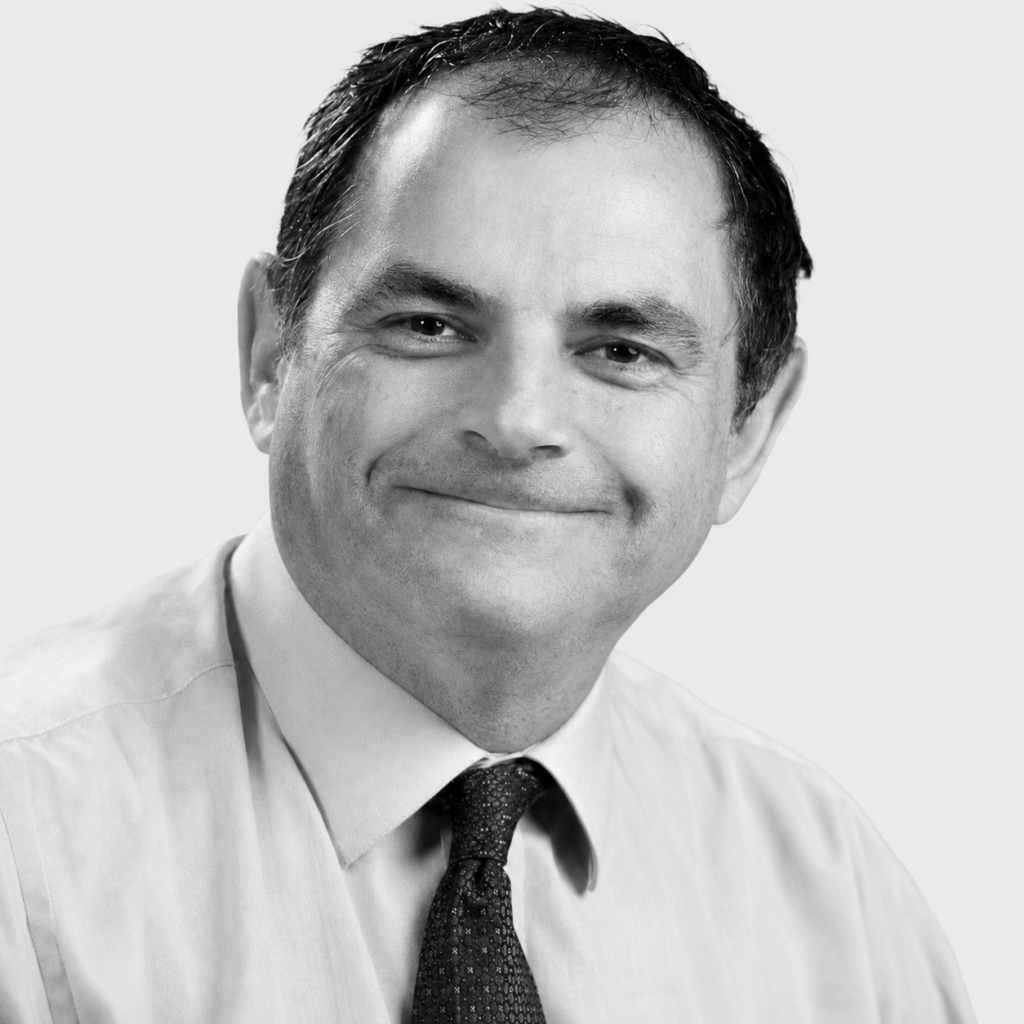 Black-and-white headshot of Huw Rees, smiling and wearing a shirt and tie.