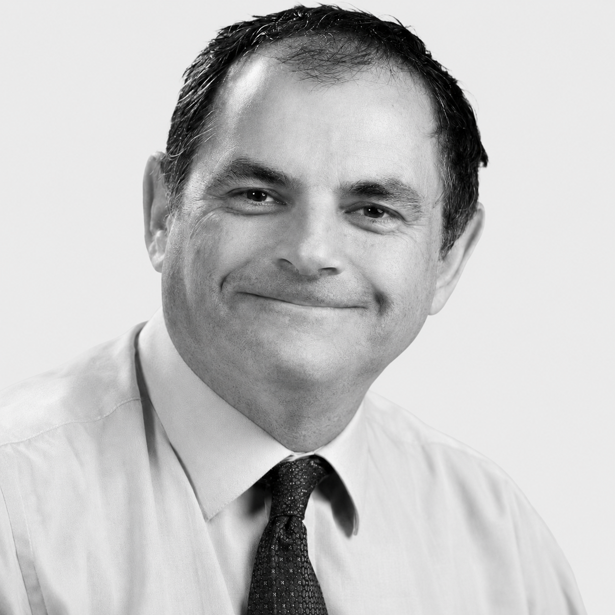 Black-and-white headshot of Huw Rees, smiling and wearing a shirt and tie.